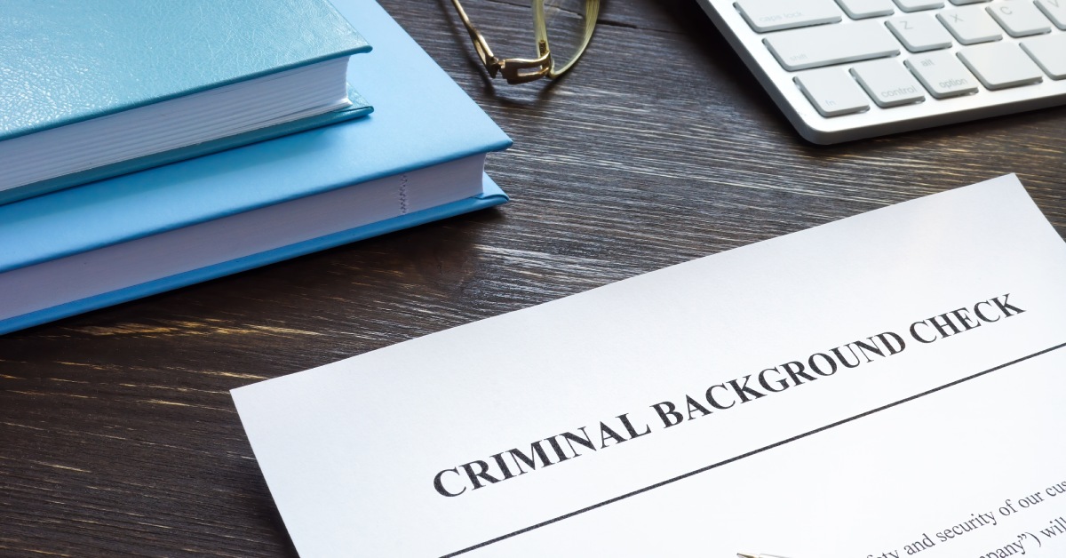 Close up a document that says "criminal background check" with a pen resting on it and eyeglasses and books above it.