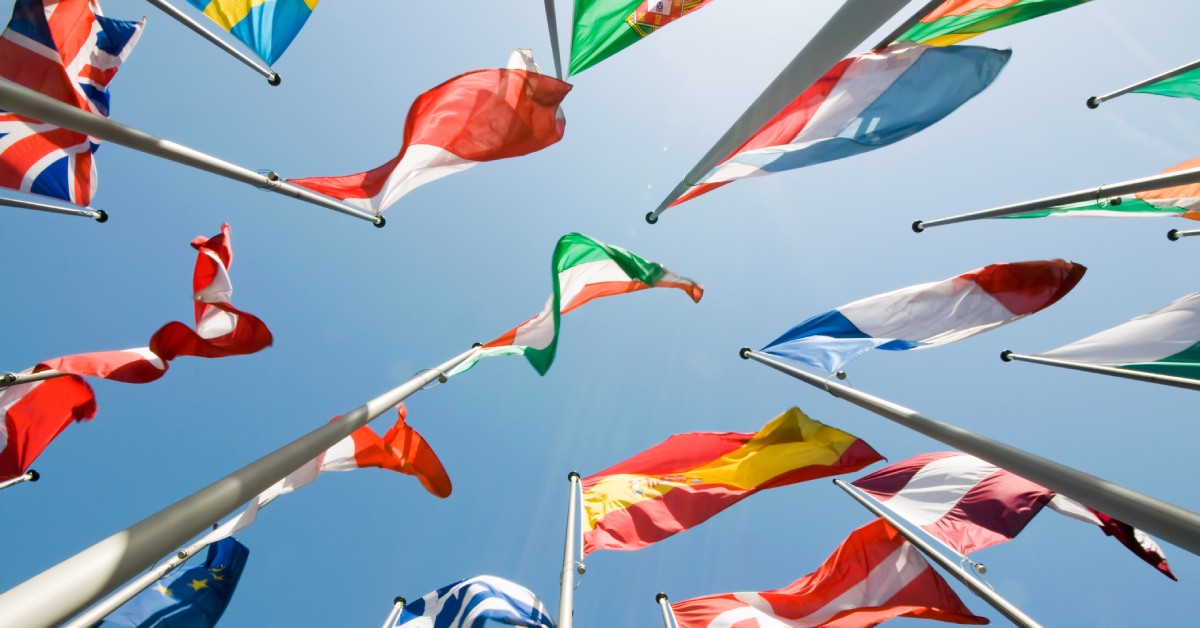 Worm's-eye view of a several flags from different countries, flapping at the top of their flagpoles.