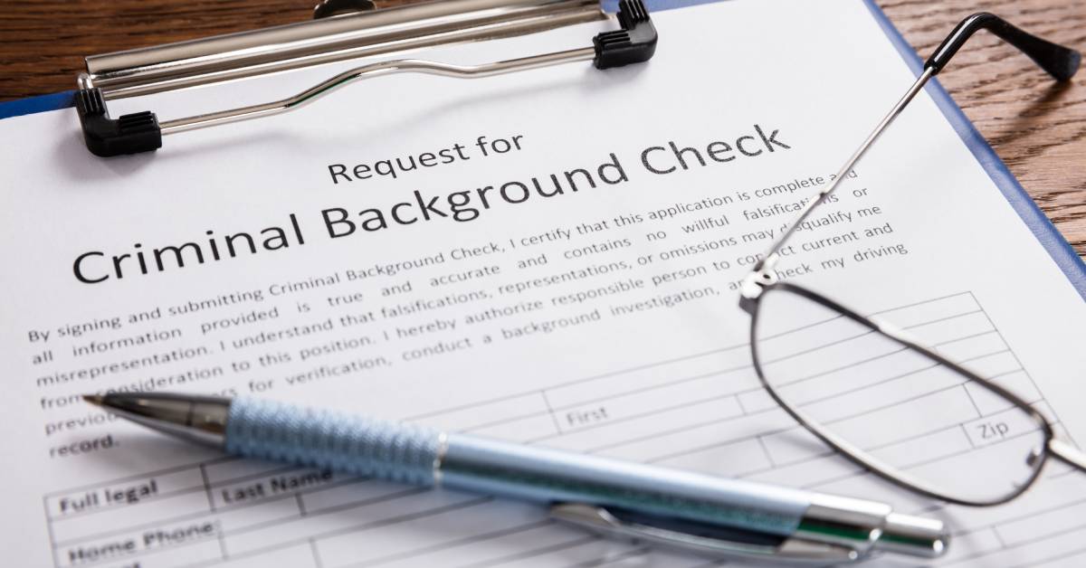 A clipboard containing a criminal background check request form with a pen and a pair of glasses on top of it.