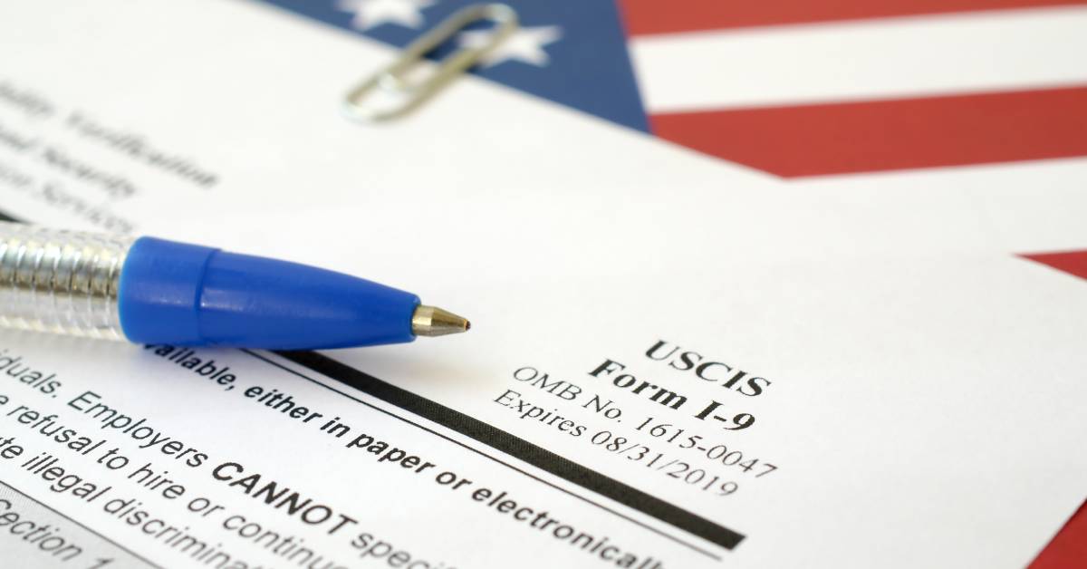 A close-up showing an I-9 verification form for employment with a blue pen on top of an American flag.