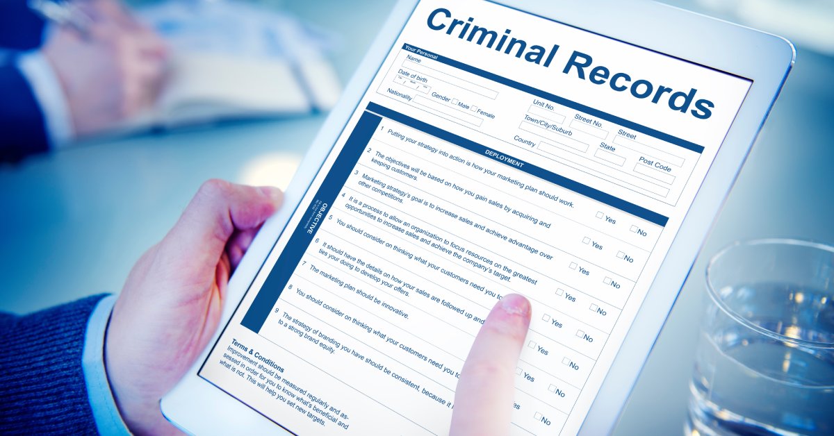 A close-up showing somebody holding a white electronic tablet that is displaying a criminal record form.
