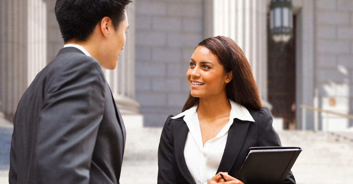 A man and a woman wearing business suits are talking to each other outside of what appears to be a government building.