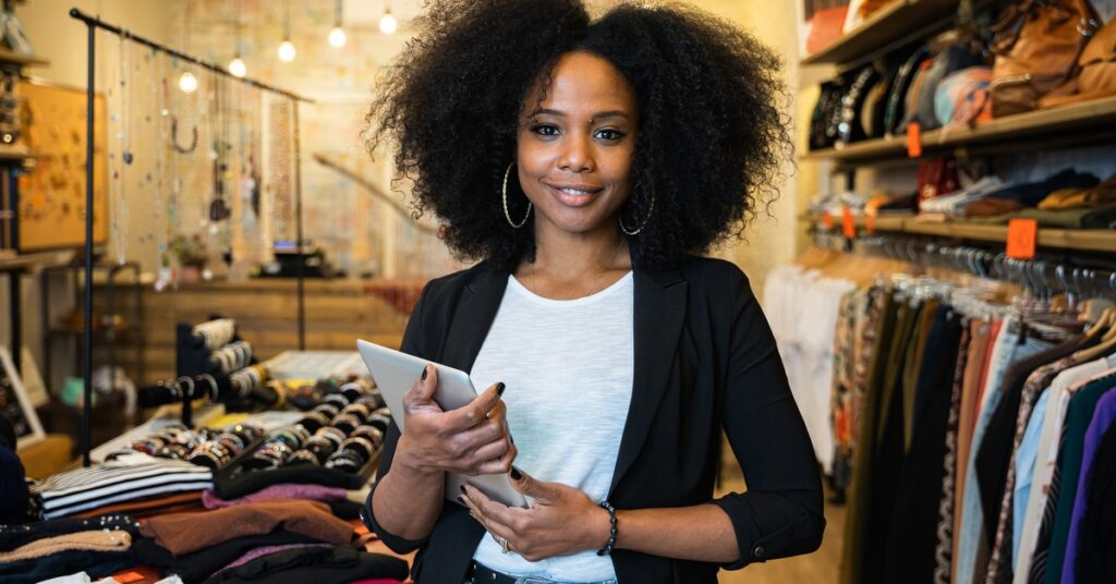 A young woman wearing a black sweater stands in front of a stack of clothing in what appears to be a store.