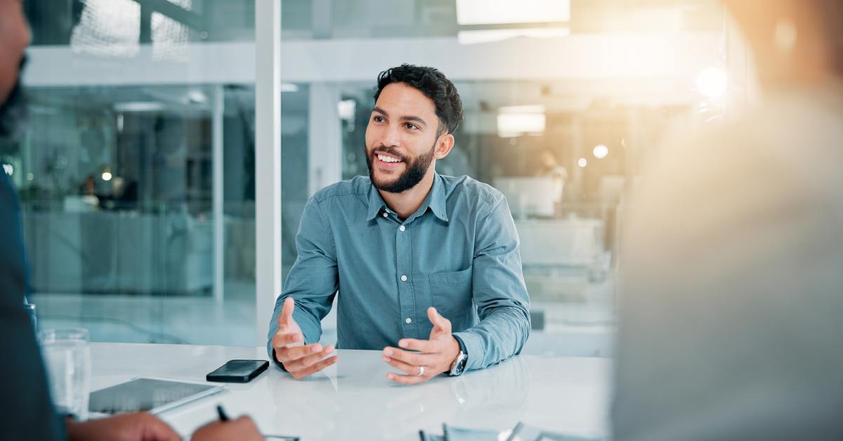 A person in a job interview speaking with the people across the table. There is office space behind the applicant.