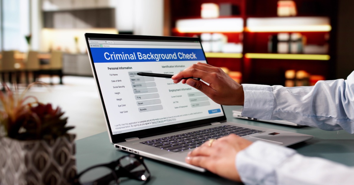 A person on a laptop reviewing a criminal background check form. They are using a pen to point at the form.