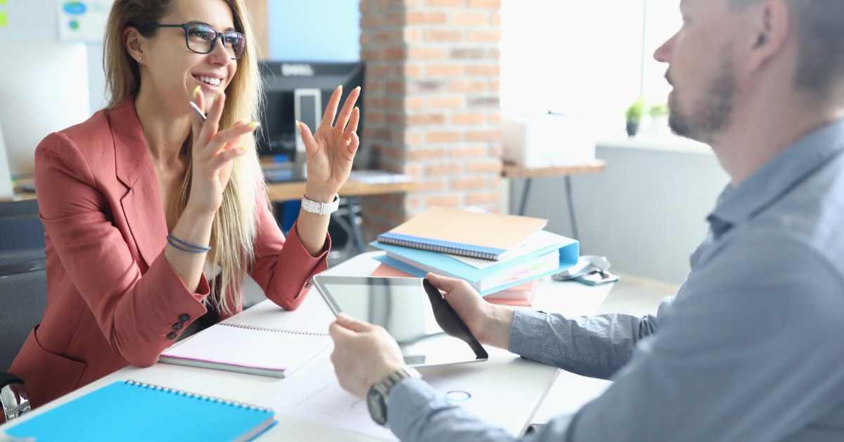 Two business people in an interview in an office setting. One of them is holding a tablet while the other speaks.
