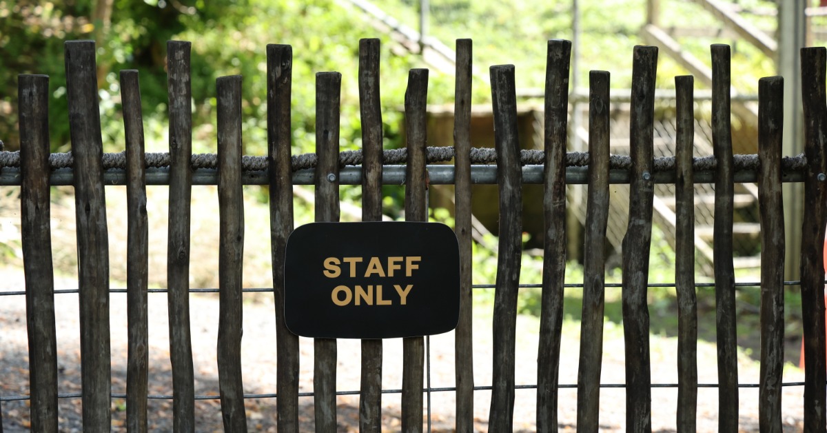 An outdoor space covered in shade with a rustic fence. Attached to the fence is a sign that says 'staff only.'