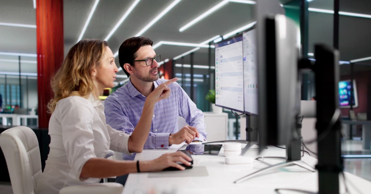 Two HR professionals sitting at an office desk together, looking at a computer to screen interview candidates.