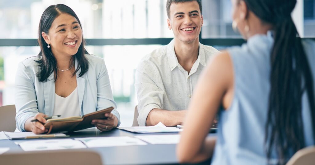 Recruitment managers in an office speaking with a potential candidate. The businessman and woman are well-dressed.